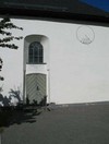 Kyrkans korportal i söder. Ett solur är målat på fasaden. Solur brukar användas på kyrkogårdar som symbol för tidens gång.
