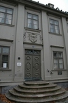 Byggnadens entré utmärks av en låg fritrappa samt ett dörröverstycke med en vapensköld