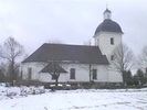 Kyrkans norra sida med sakristia. Kyrkan är omgiven av kyrkogården och en trädkrans av lind.