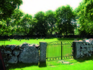 Kyrkogårdens enda ingång. Den konstfulla smidesgrinden
i norr. Längs muren växer trädkransen av lönnar.