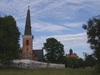 Ängsö kyrka och kyrkogård med omgivande mur i förgrunden och i bakgrunden skymtar Ängsö Slott. 