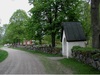 Vägen mot Hjälmare kanal passerar norra kyrkogårdsmuren, där enda stigluckan finns.  med stiglucka. I bakgrunden ses ett skolhus från 1910-talet. Digitalfoto Rolf Hammarskiöld 2002