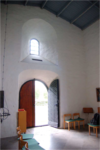 Kapellets entré under fönsternischen som ursprungligen var rummets enda. De nuvarande lösa inventarierna är samlade från olika ställen och saknar koppling till kapellet.