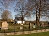 Kyrkogårdens sydvästra hörn med gjutjärnsstaketet på sin terrasskant, delar av trädkransen samt
gravkapellet.