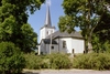 Vänersnäs kyrka är inbäddad i ymnig vegetation med gamla askar längs murkrönet.