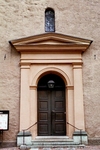 Västra porten i Vänersborgs kyrka har en tidstypisk, arkitektonisk uppbyggnad likt en tempelgavel. Dörrbladen är klädda med kopparplåt.