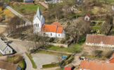 Flygbild över Västra Nöbbelövs kyrkoanläggningen, tagen från sydost. Till höger ligger den f d prästgården, uppförd 1816.