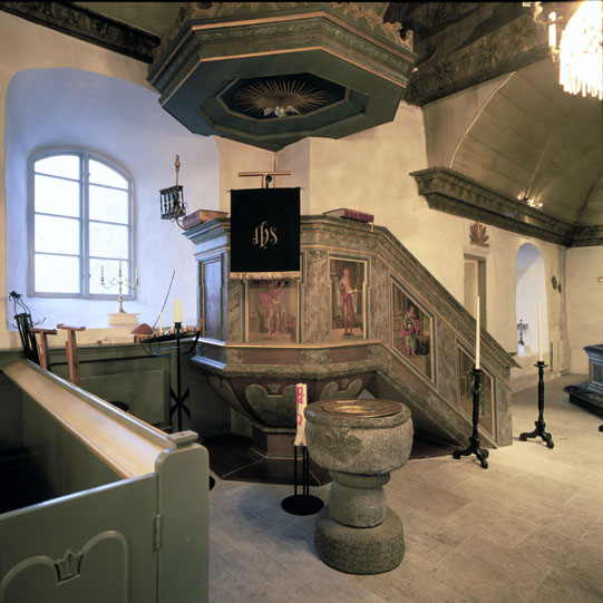 Predikstolen och dopfunten. Predikstolens korg är från 1600-talet (basen ersatt) och ljudtaket från 1700-talet.