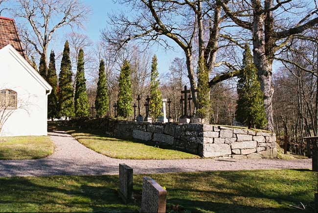 Öster om kyrkan syns Ekmanska gravplatsen med ett femtontal smidda järnkors. Sedd från söder. 