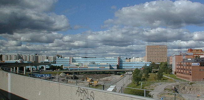 Kista Centrums blå byggnadskomplex ligger som en bro mellan bostadsområdet till vänster och arbetsplatsområdet till höger. SAK12139 Sthlm, Kista, Danmark 1, Kista Torg 4, från tunnelbanevagn , SO 


