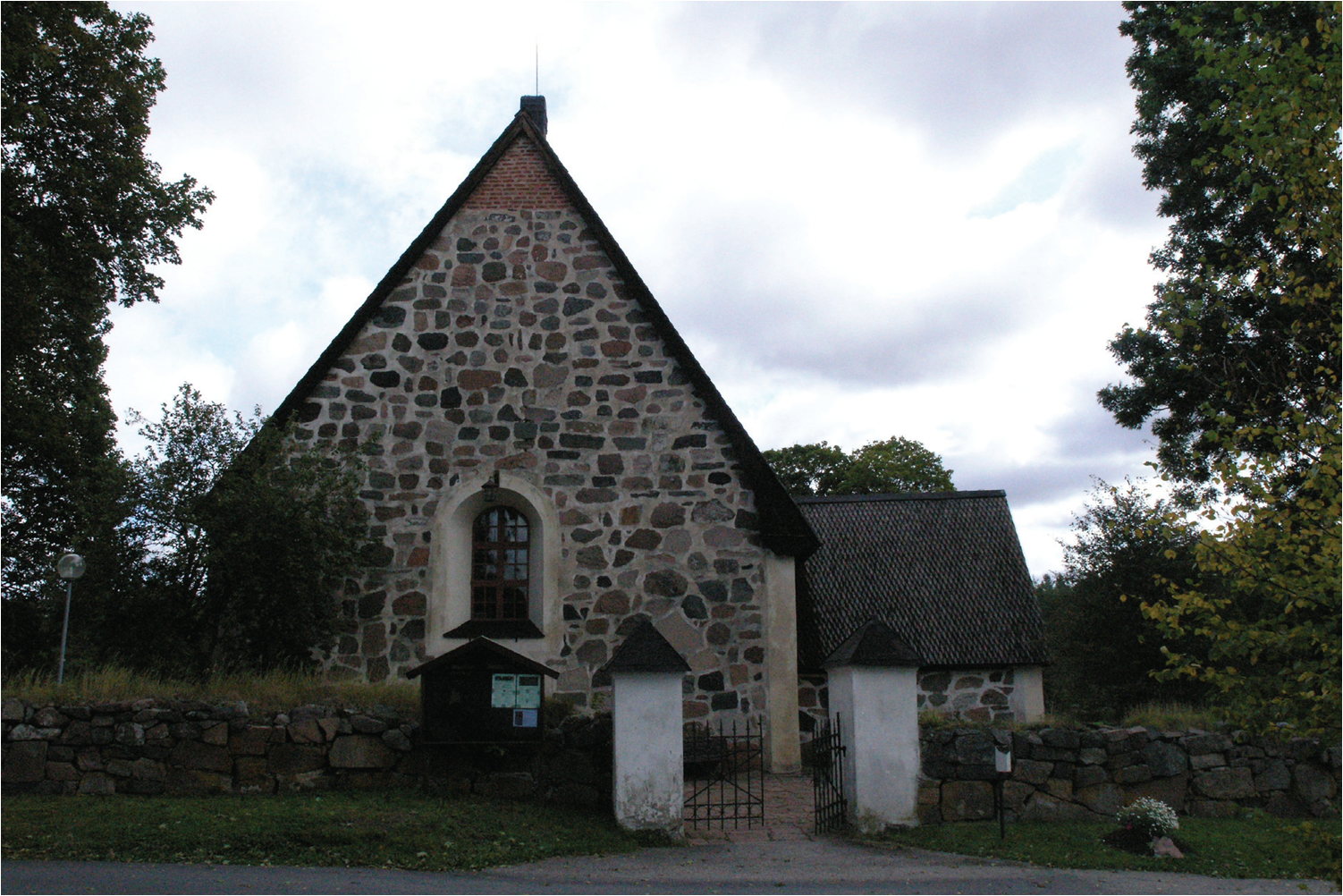 Häverö kyrka sedd från väster, med huvudentré genom den äldsta kyrkogårdsmuren.
