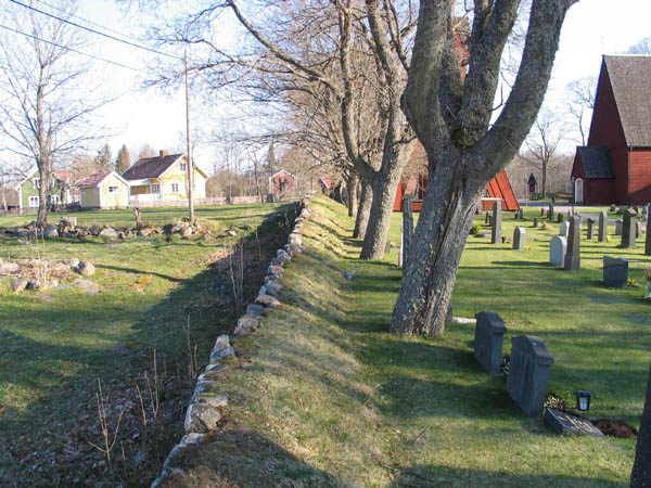 Kyrkogårdens stödmur och trädkrans i väster.