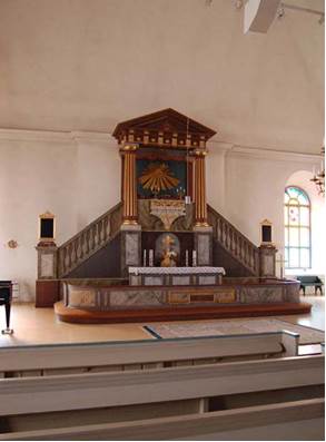 Det högvälvda och enkla kyrkorummet domineras av den pampiga altarpredikstolen. 