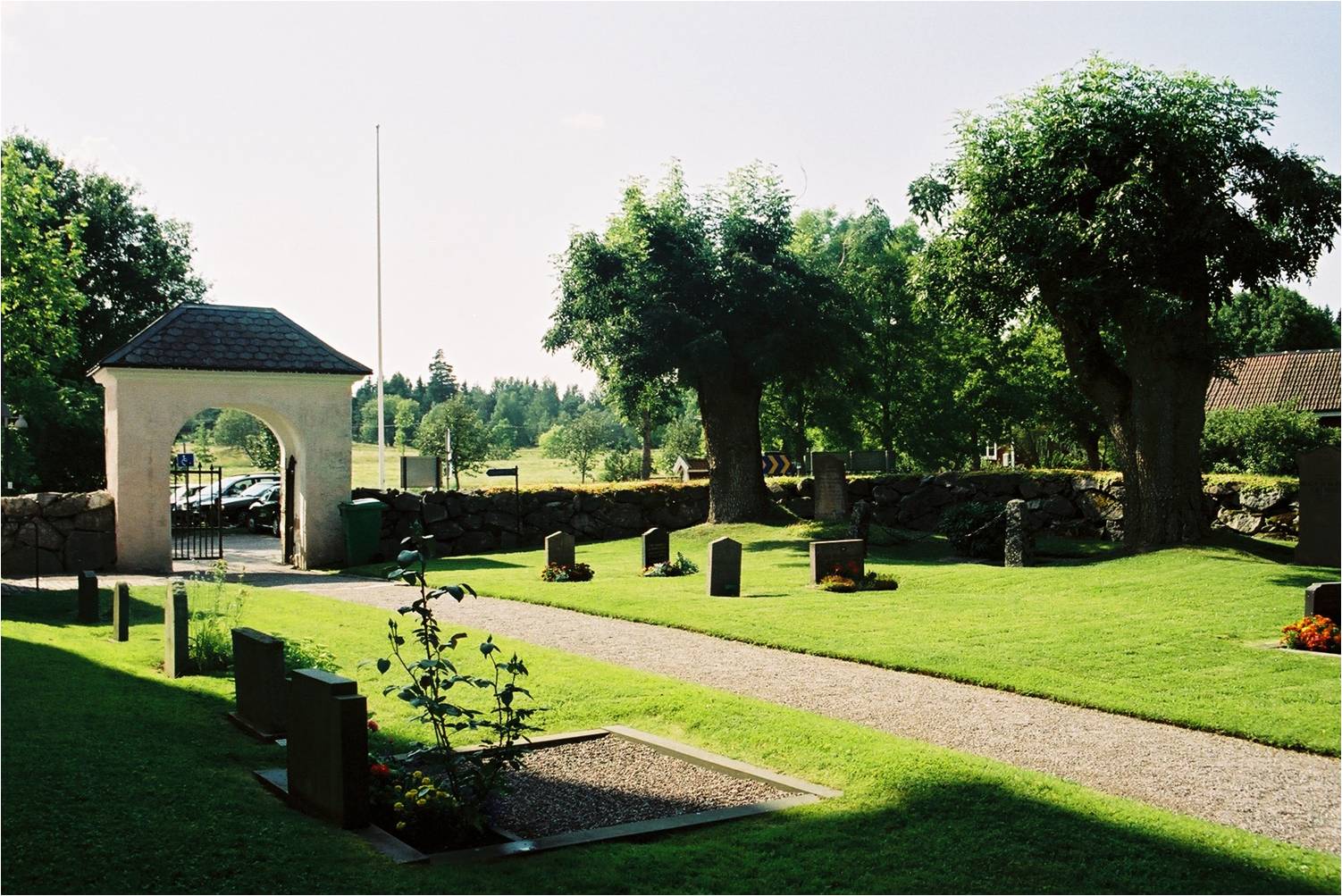 Västra Ryds kyrkogård söder om kyrkan med stiglucka och äldre träd.
