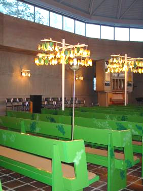 Interiör med kyrkorummets ljusträd och ”lövskuggade” bänkar