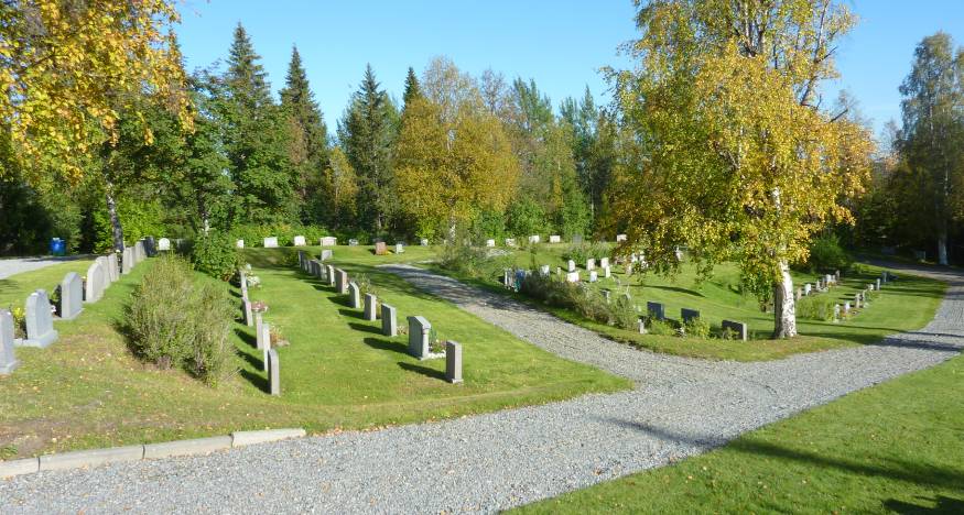 Kyrkogården mot sydost. Den är terrasserad och gräsbevuxen, med en grusgång som leder runt den och ljusa, låga stående gravstenar i prydliga rader.