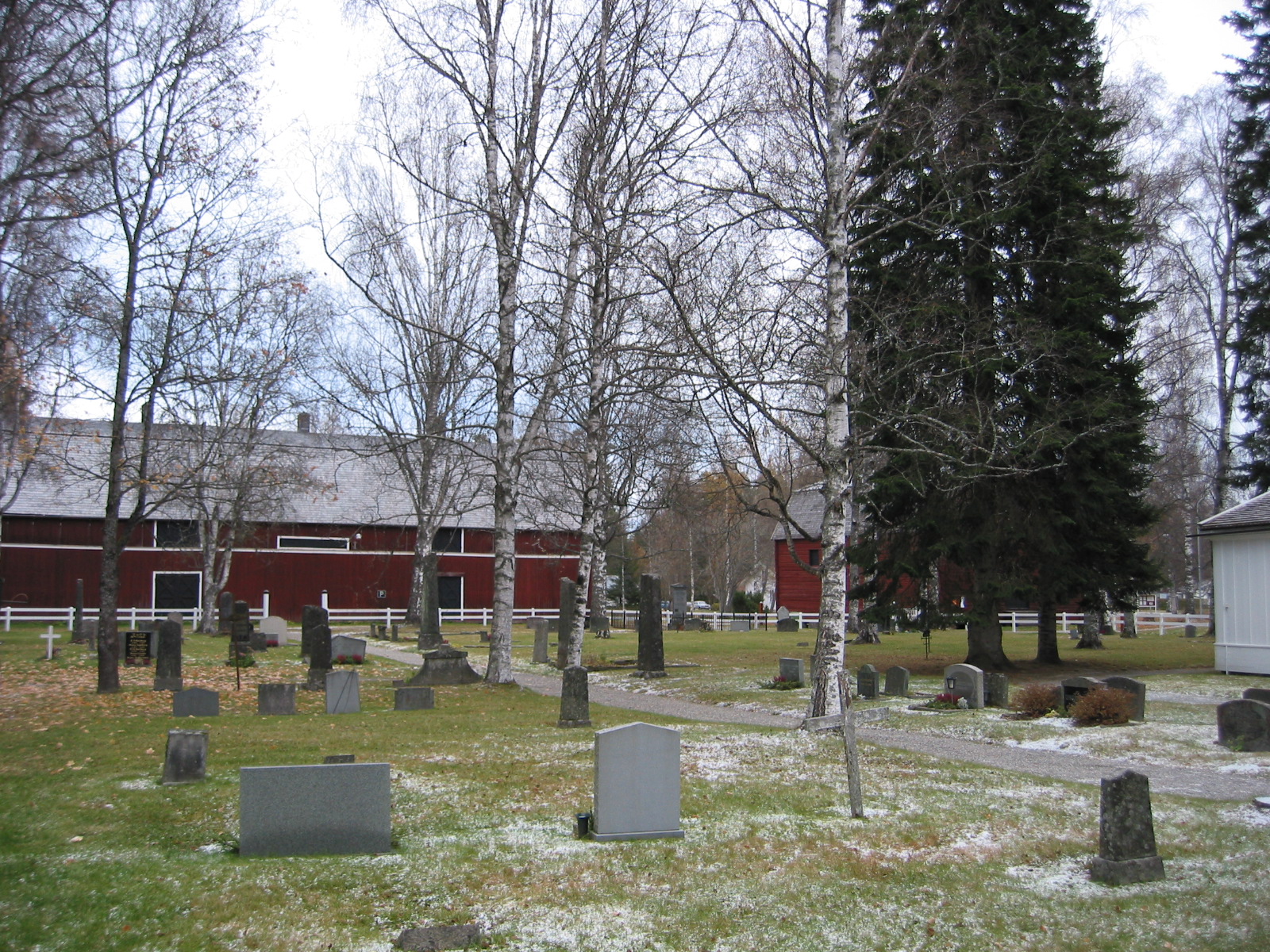 Lögdö kyrka/Lögdö brukskapell, kyrkogården, i bakgrunden skymtar ladugården och det timrade magasinet i öster, vy från väster. 