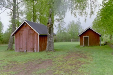 Intill sydvästra kyrkogårdsmurens utsida står dessa två små ekonomibyggnader till Tämta kyrka, vid en fotbollsplan.