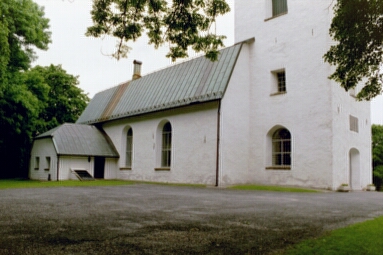 Toarps kyrka med sakristian sedd från nordväst och parkeringen i förgrunden.