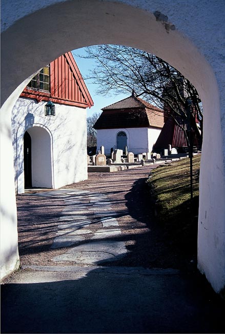 Ingången till kyrkan sedd genom stigluckan. Längst bort det Almrothska gravkoret.