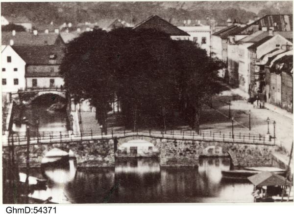 Gamla Lejonbron (byggd 1733) fotograferad år 1863, strax innan den revs våren 1864. Där bakom syns Brunnsparken och taket på gamla Sockerbruket sticker upp. Kanalen söder om Brunnsparken har nyss fyllts igen. Därmed är inte platsens ursprung på en holme i Stora Hamnkanalen längre synlig. Till vänster om sockerbruket välver sig Slusskvarnen, byggd 1648, över kanalen (riven 1873).
GhmD:54371